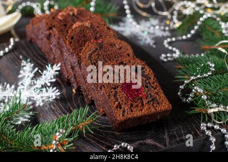 Cupcake natalizio a fette con ciliegie e cioccolato ricoperti di glassa al cioccolato su tavola di legno su sfondo di Capodanno Foto Stock