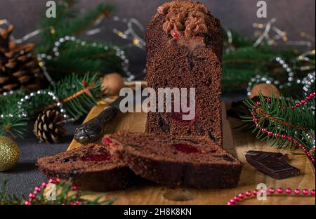 Cupcake natalizio a fette con ciliegie e cioccolato ricoperti di glassa al cioccolato su tavola di legno su sfondo di Capodanno, primo piano Foto Stock