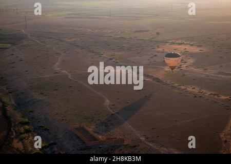 Un ballon d'aria calda e la sua lunga ombra all'alba nel deserto del Marocco, un tour vicino Marrakech. Foto Stock