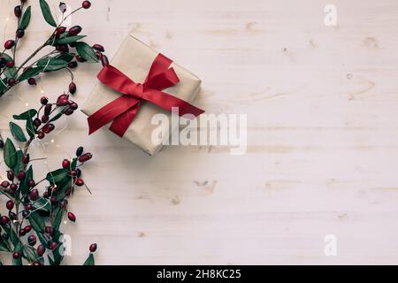 Un regalo di Natale con arco a nastro rosso dall'alto con un bordo di acini rossi e mini luci natalizie su sfondo bianco con spazio copia Foto Stock