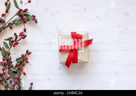 Un regalo di Natale con arco a nastro rosso dall'alto con un bordo di acini rossi e mini luci natalizie su sfondo bianco con spazio copia Foto Stock