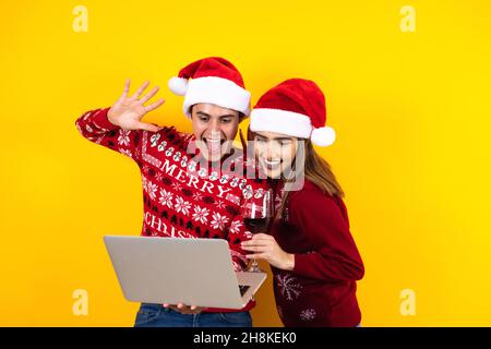 giovane coppia latina con videochiamata di natale utilizzando un tablet digitale o un touchpad su sfondo giallo in america latina Foto Stock