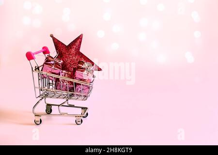 Carrello supermercato con regali confezionati in carta rosa, una stella di Natale. Colori dell'anno 2022. colore rosa pacifico. Campagna regalo per lo shopping di Capodanno Foto Stock