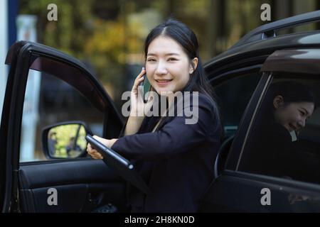 Donne di lavoro intelligenti che hanno un colloquio di affari al telefono mentre escono dall'automobile. Concetto occupato delle donne di affari. Foto Stock