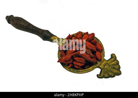 Berries rosso goji (essiccato) in vecchio cucchiaio di ottone isolato su sfondo bianco con percorso di taglio. Messa a fuoco selettiva. Foto Stock