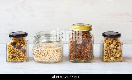 Vasetti pieni di avena e vari granoli croccanti - frutta secca, frutta secca, noci e cioccolato. Concetto di mangiare sano. Foto Stock