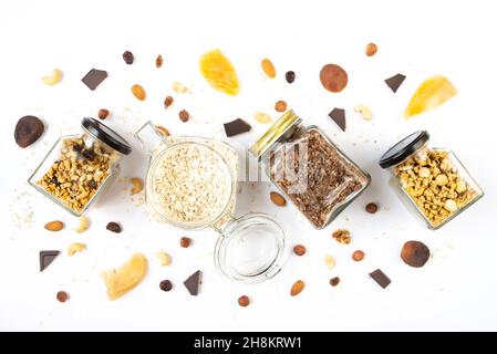 Vista dall'alto di vasetti pieni di avena e vari granoli croccanti con ingredienti sparsi intorno - frutta secca, noci e barrette di cioccolato. Salute mangiare con Foto Stock