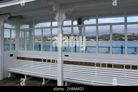 Primo piano di posti a sedere e riparo sul Molo Swanage, Dorset, Inghilterra con la città sullo sfondo. Foto Stock