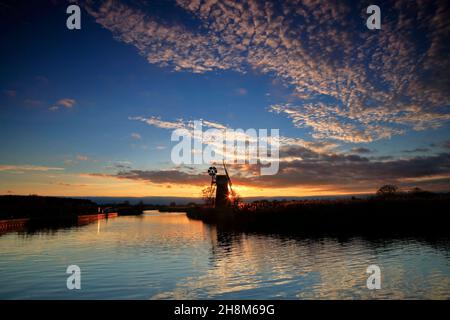 Un tramonto sul fiume ANT sulle Norfolk Broads con mulino a vento e riflessi in autunno a Ludham, Norfolk, Inghilterra, Regno Unito. Foto Stock