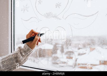 Femmina dipinto a mano cervo di Natale dipinto su vetro della finestra. Decorazioni invernali di Natale sul vetro della finestra. Motivo bianco del cervo. Tracciatura dell'arte della neve Foto Stock