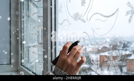 Femmina dipinto a mano cervo di Natale dipinto su vetro della finestra. Decorazioni invernali di Natale sul vetro della finestra. Motivo bianco del cervo. Tracciatura dell'arte della neve Foto Stock