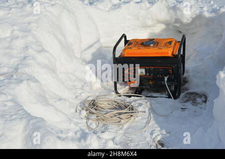 Un generatore portatile, un generatore di energia di riserva intorno alla neve dopo il clima invernale intenso, la neve e la tempesta di neve. Usando un generatore mobile per fornire il pow Foto Stock