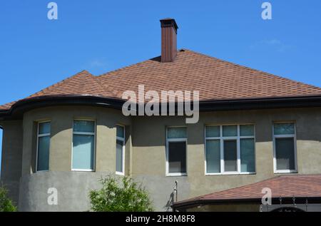 Una casa incompleta in costruzione con una parete semicircolare in stucco intonacata con finestre a bovindo, e il tetto coperto con tegole da copertura in asfalto Foto Stock