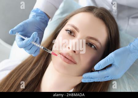 La giovane donna viene iniettata di botox nelle sue labbra, cosmetologa usando la siringa Foto Stock