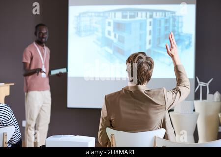 Vista posteriore dell'uomo d'affari che solleva il braccio mentre si siede alla presentazione di affari davanti al grande monitor Foto Stock