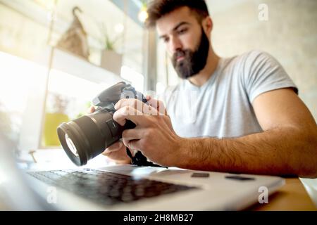 Giovane fotografo che regola le impostazioni sulla sua fotocamera. Preparazione del ritocco delle foto sul computer. Foto Stock