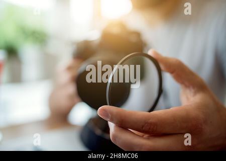 Giovane fotografo che regola le impostazioni sulla sua fotocamera. Mettendo un filtro di vetro sul suo obiettivo, preparandosi per la sessione di foto. Foto Stock
