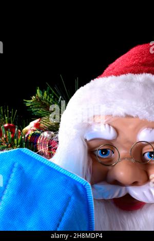 Foto di Babbo Natale con decorazioni natalizie sullo sfondo e una maschera blu fuori fuoco in primo piano. La foto è destinata a ricordare Foto Stock