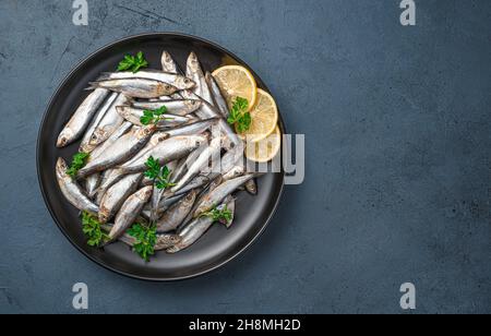 Un piatto pieno di sardine con limone e prezzemolo su sfondo blu scuro. Vista dall'alto, spazio di copia. Pesce di mare. Foto Stock