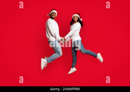 Bella coppia nera in Babbo Natale cappelli tenere le mani e saltare Foto Stock