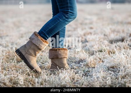 Donna che indossa stivali in pelle con pelliccia in inverno. Camminare all'aperto in hoarfrost. Gambe femminili con jeans skinny. Foto Stock