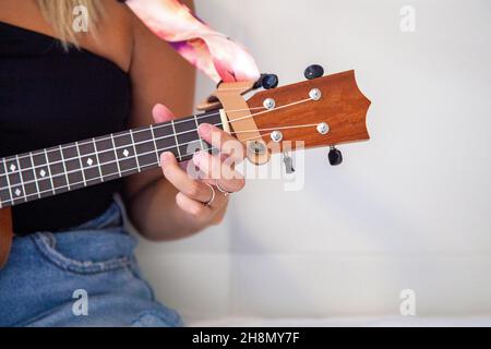 Donna che gioca l'ukulele seduto sul letto nella sua stanza a casa. Foto Stock