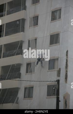salvador, bahia, brasile - 30 novembre 2021: Lavoratore di costruzione appeso con corde su una facciata di un edificio durante le riparazioni di costruzione in città Foto Stock
