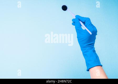 Mano nel guanto blu che regge lo specchio dentale Foto Stock