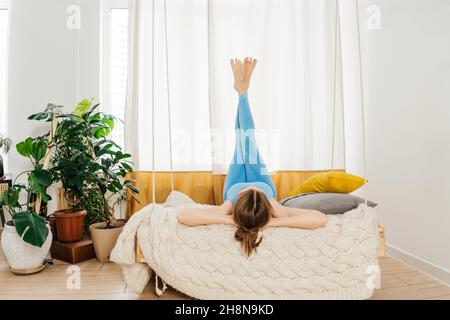Giovane donna rilassarsi in swing indoor. Lei si trova sulla schiena, gambe su. Foto Stock