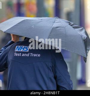 Uomo che indossa giacca NHS Test & Trace. Negozi di Natale, negozi per lo shopping in una giornata bagnata e ventosa nel centro della città. La pioggia del mattino si sciolgerà verso sud, ma i venti da freschi a moderati verso nord persisteranno aggiungendo un notevole fattore di raffreddamento. Southport, Lancashire. Meteo Regno Unito Dicembre 2021. Foto Stock