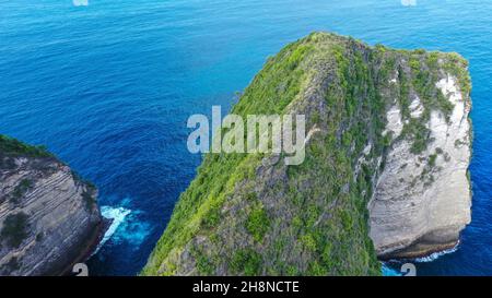 Vista aerea dell'ipnotizzante e panoramica Kelingking Beach con una scogliera a strapiombo e un promontorio coperto di verde denso bagnato dalle acque turchesi del mare su un sole Foto Stock