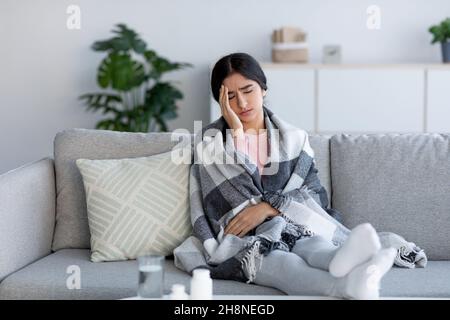Stanco triste turbata giovane donna indù avvolto in plaid, che soffre di mal di testa e influenza, siede sul divano Foto Stock