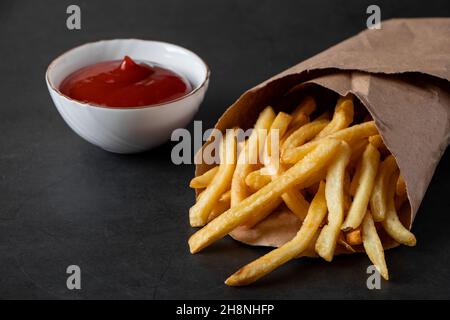 Patatine croccanti calde in un sacchetto di carta su sfondo nero. Gustoso fast food americano. Foto Stock