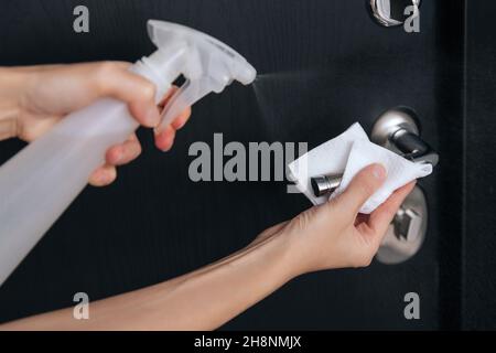 Pulizia delle maniglie nere delle portiere con un panno antisettico umido. Donna mano che usa un asciugamano per pulire la porta della stanza di casa link. Igienizzare le superfici in Foto Stock