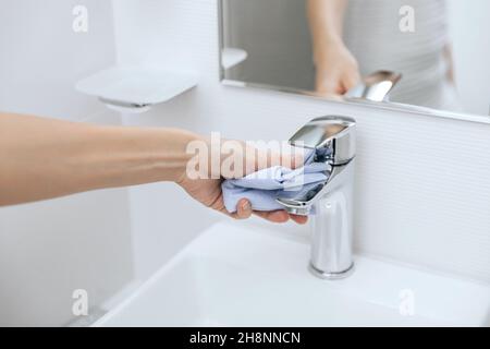 Pulire il rubinetto del lavello con un panno in microfibra. Pulizia del bagno. Igienizzare le superfici di prevenzione in ospedale e spazi pubblici contro corona Foto Stock