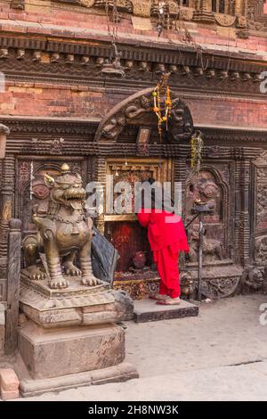 Una donna nepalese che indossa un kameez rosso salwar adorando al tempio di Bhairab Nath a Bhaktapur, Nepal. Foto Stock