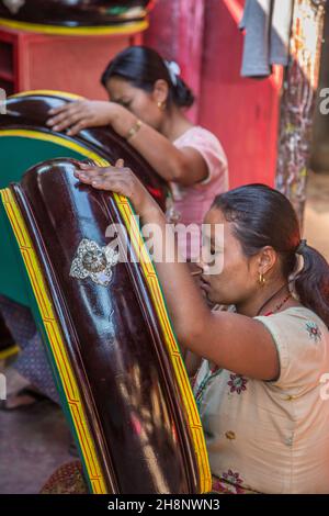 Due donne dipingendo tamburi rituali tibetani in un laboratorio all'aperto a Kathmandu, Nepal. Foto Stock