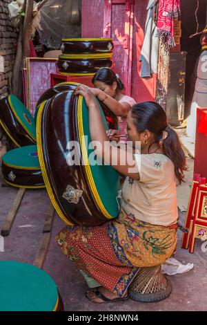 Due donne dipingendo tamburi rituali tibetani in un laboratorio all'aperto a Kathmandu, Nepal. Foto Stock