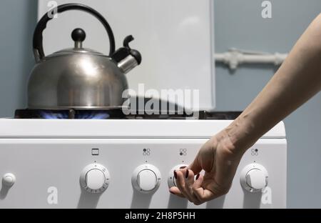 una persona aggiunge gas sul fornello dove si trova il bollitore. Foto di alta qualità Foto Stock