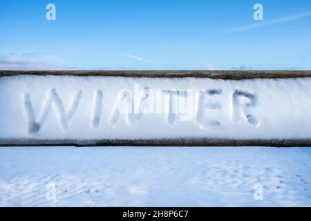 La parola 'inverno' scritta a mano nella neve su un asse di legno in una giornata invernale soleggiata. Campo innevato incontaminato e cielo blu sullo sfondo. Concetto invernale Foto Stock