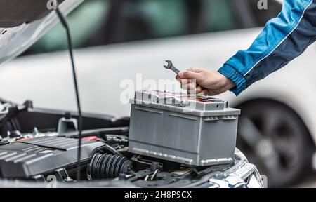 Il meccanico tiene la chiave sulla batteria dell'auto con il vano motore aperto. Foto Stock