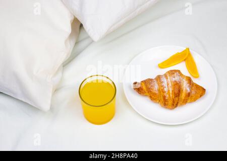 Succo d'arancia fresco e croissant sul letto. Mattina colazione minima a letto. Foto Stock