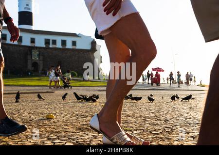 Vista dal basso di Farol da barra in Salvador, con piccioni che mangiano mais a terra e turisti che passeggiando. Foto Stock