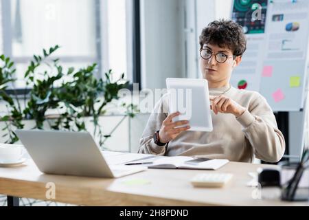 uomo d'affari che utilizza un tablet digitale vicino a dispositivi e caffè in ufficio, immagine stock Foto Stock