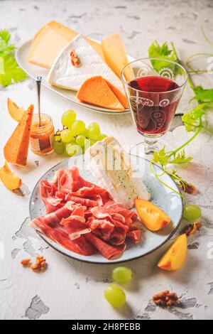 Piatto di prosciutto e formaggio con uva, noci e vino rosso Foto Stock