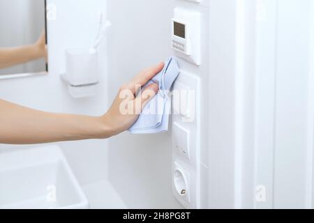 Pulizia di interruttori e prese con un panno in microfibra. Sanitizzare la prevenzione delle superfici in ospedale e spazi pubblici contro il virus corona. Mano della donna Foto Stock