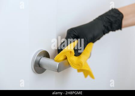 Pulizia della maniglia dello sportello con panno giallo in guanti neri. Donna mano che usa un asciugamano per la pulizia. Disinfezione in ospedale e spazi pubblici contro corona Foto Stock