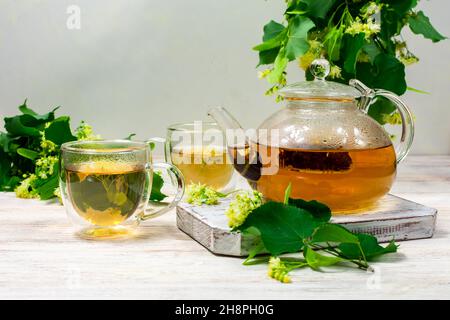 Teiera e due tazze di tè con un tiglio su un tavolo di legno. Tè healing. Foto Stock