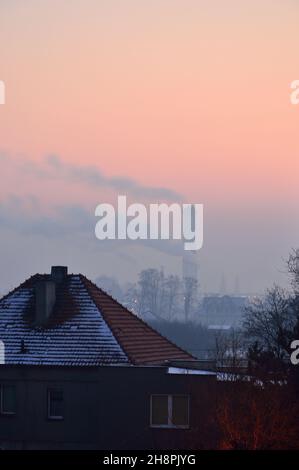 Smoking chimneys and roofs of multi-family houses against the rising sun on a winter day. Winter. Foto Stock