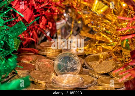 Pila di monete con un euro davanti e con decorazioni natalizie intorno Foto Stock